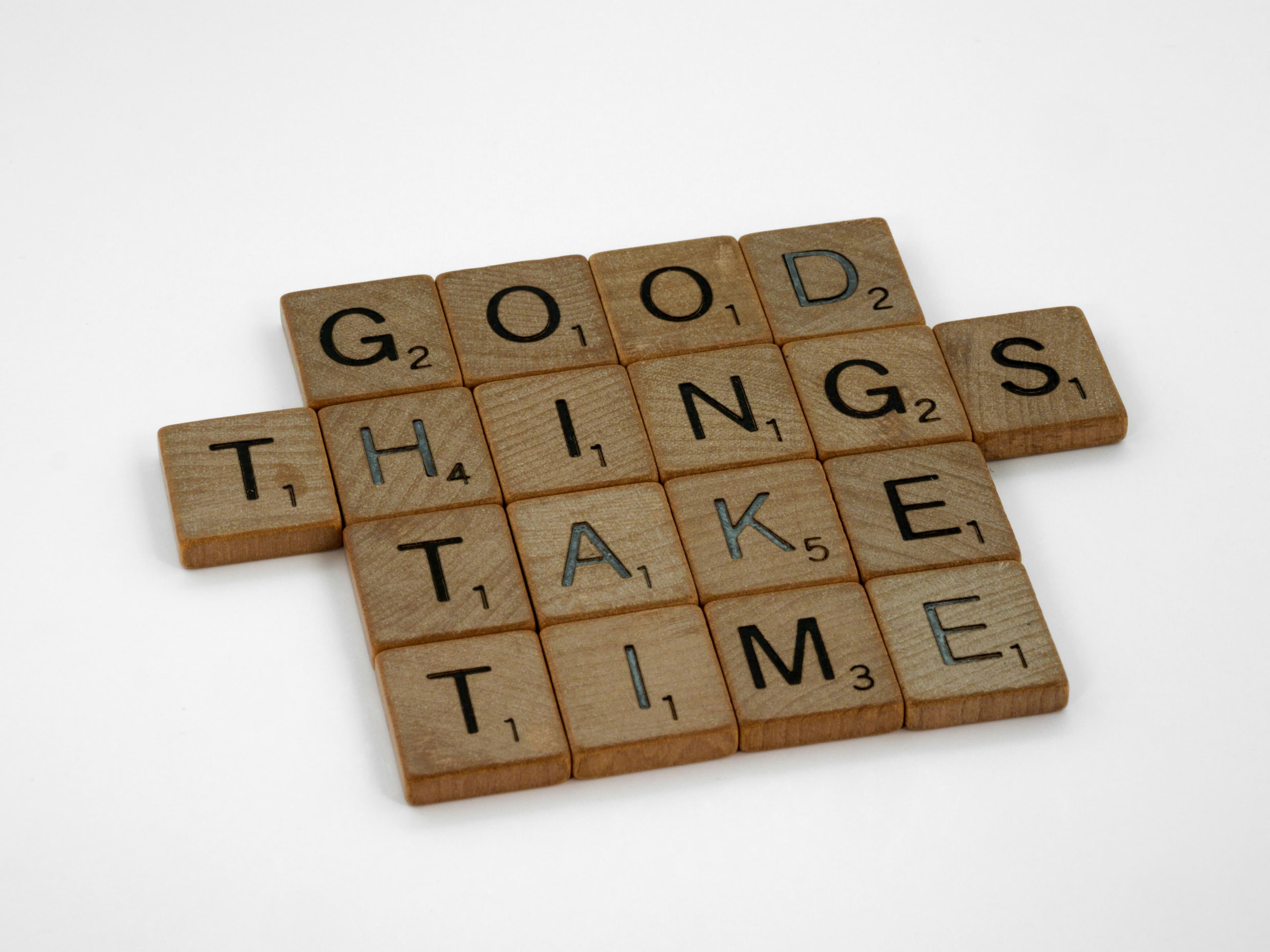 Wooden letter tiles spelling "GOOD THINGS TAKE TIME" on a plain white background.