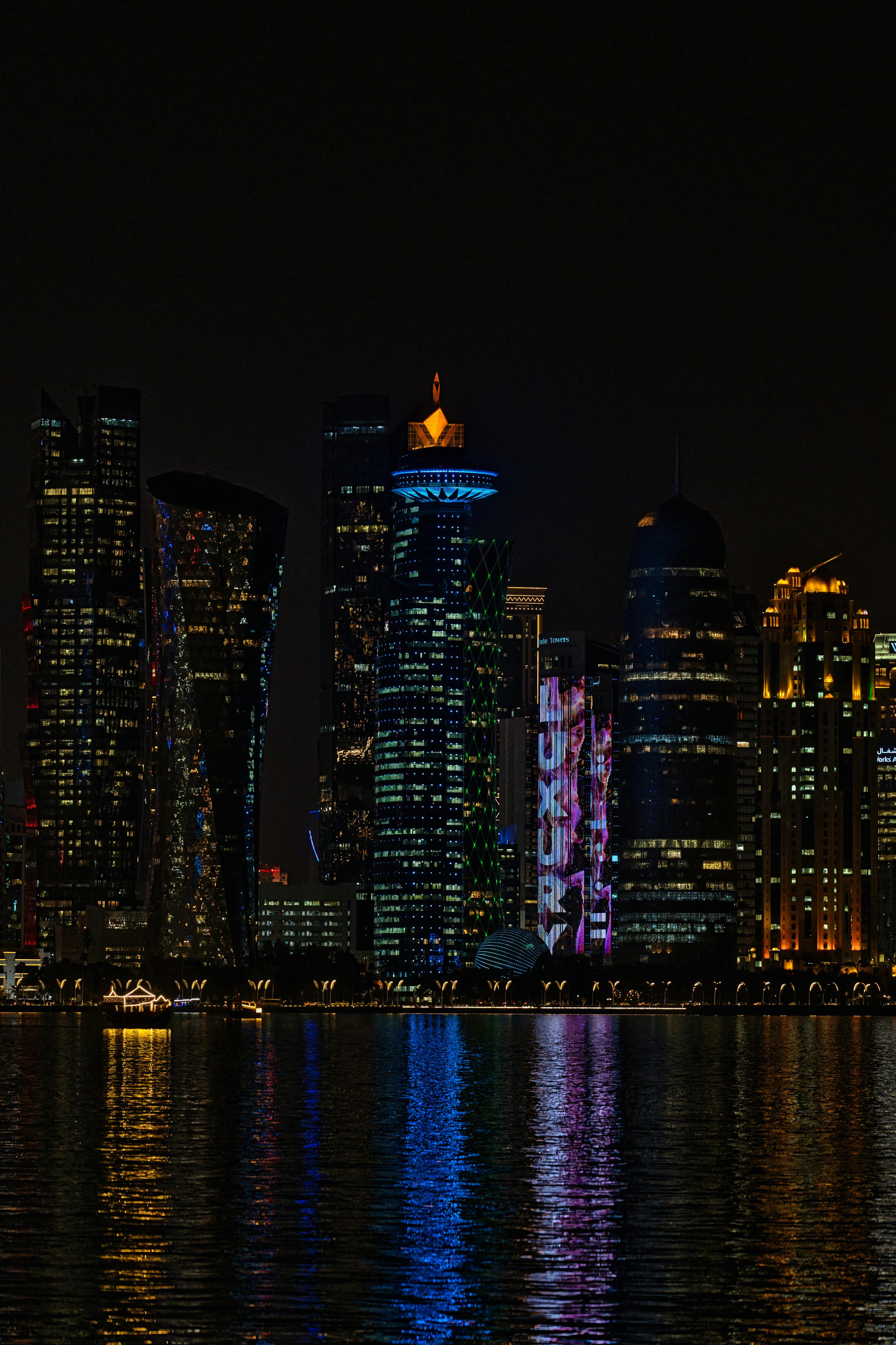 Colorful illuminated skyscrapers of a city skyline at night reflected in the calm dark water.